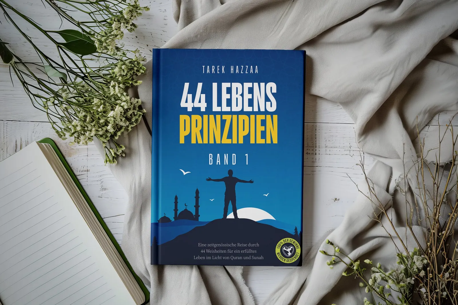 Buchcover „44 Lebensprinzipien“ auf einem hellen Tuch mit Notizbuch und Blumen